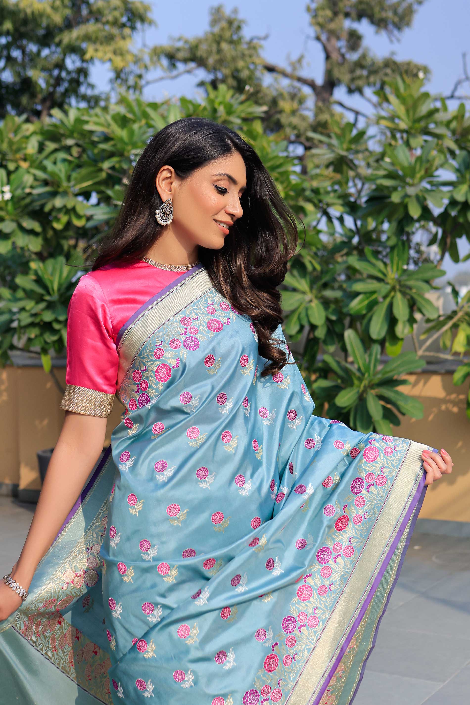 Woman wearing a light blue saree with pink floral patterns outdoors.