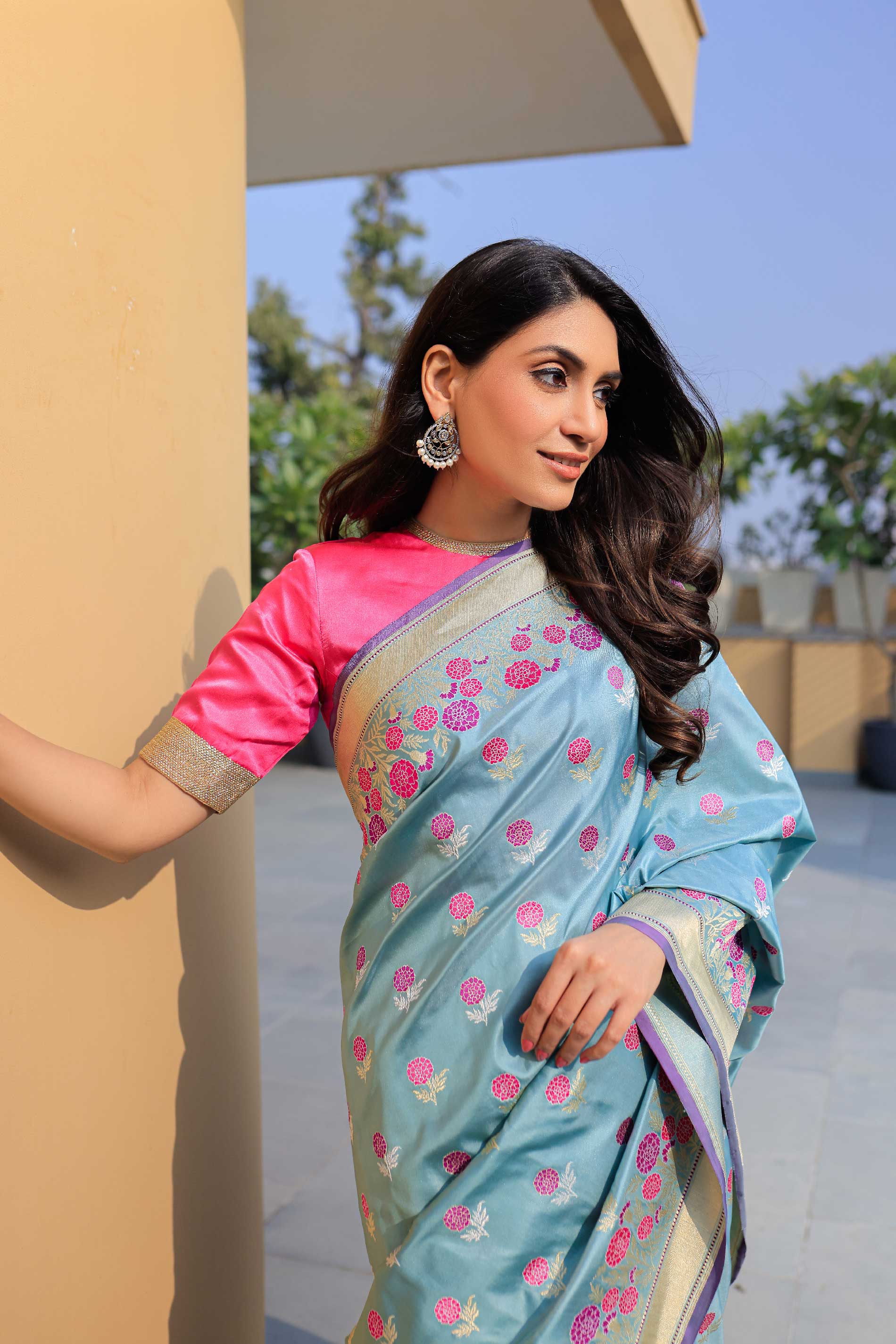 Woman wearing a light blue saree with pink blouse, standing outdoors.