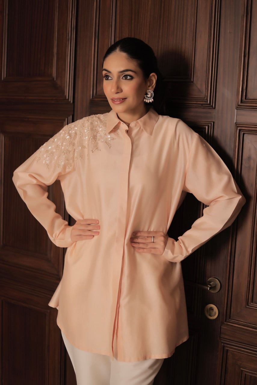 Woman wearing a light pink blouse with intricate designs against a wooden panel background