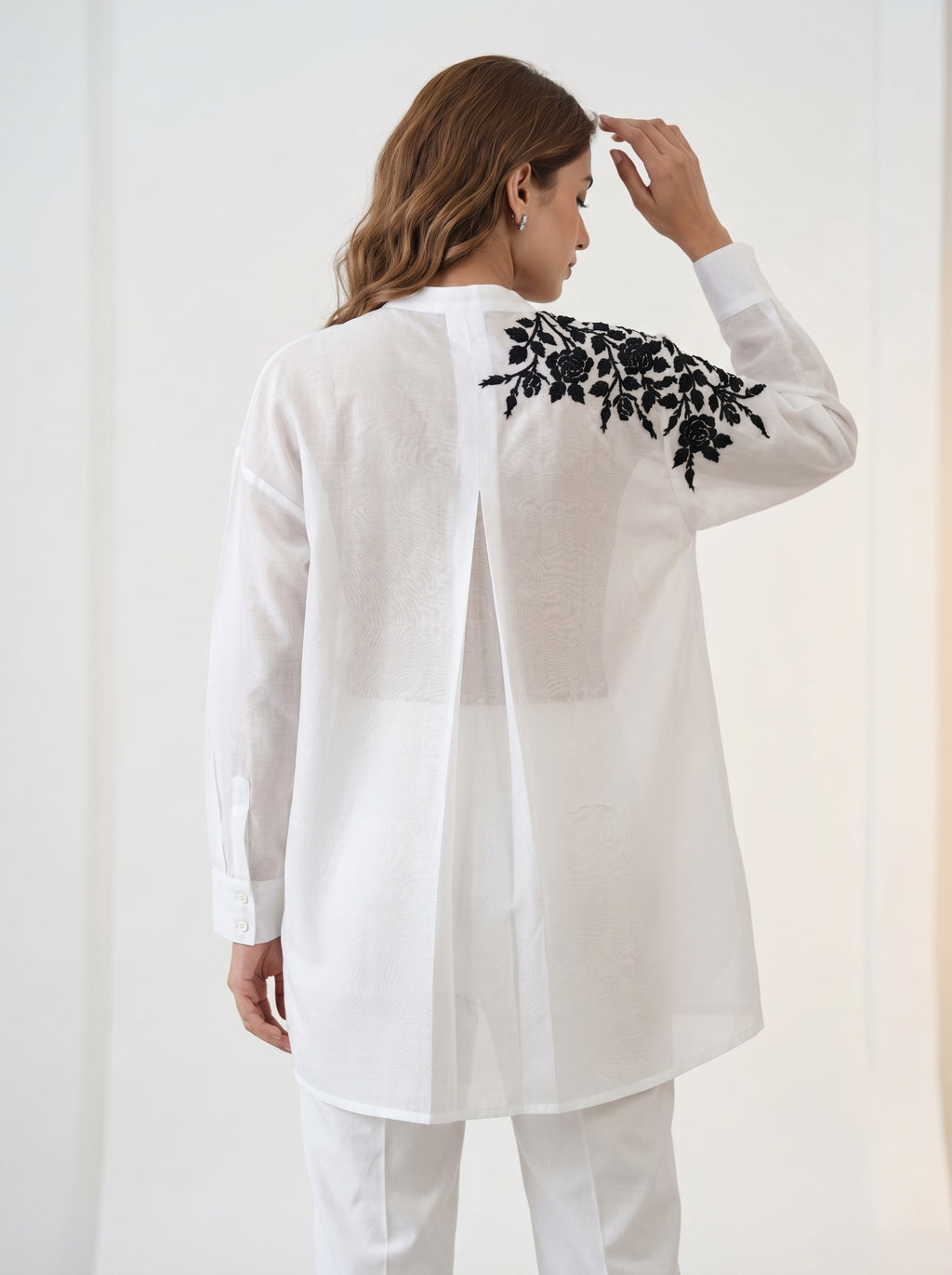 Woman wearing a white outfit with black floral embroidery on a plain background